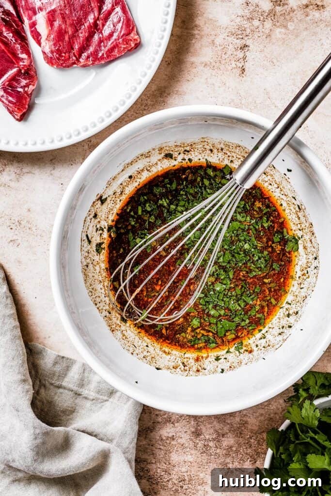 A white mixing bowl with dark-brown marinade and a whisk resting in it.