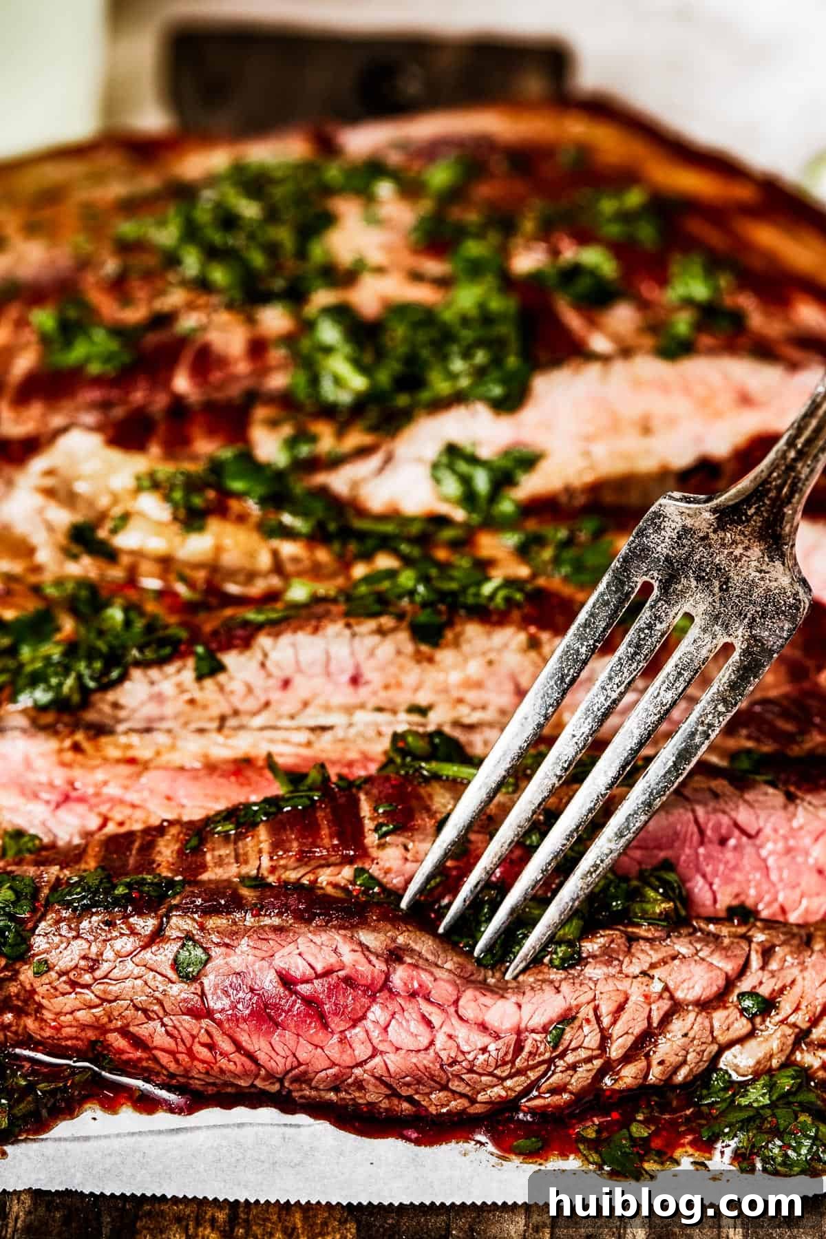 Side view of tender, sliced flank steak with a fork, emphasizing its juicy texture.