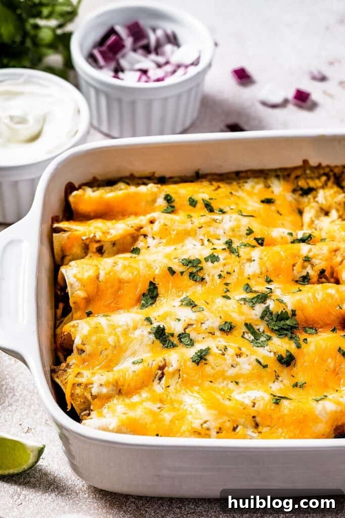 A white baking dish of freshly baked salsa verde chicken enchiladas, presented alongside a small bowl of sour cream and a bowl of finely chopped red onion for topping.