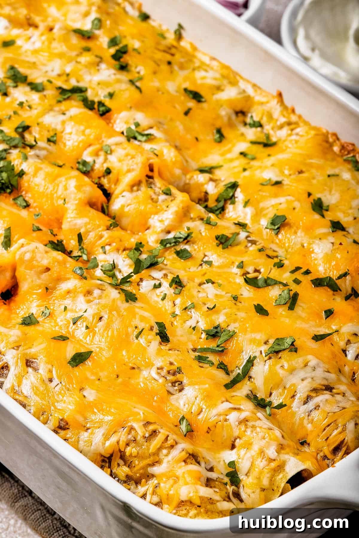 Close-up of a white baking dish filled with cheesy salsa verde chicken enchiladas, garnished with fresh, chopped cilantro, showing the bubbling sauce and melted cheese.