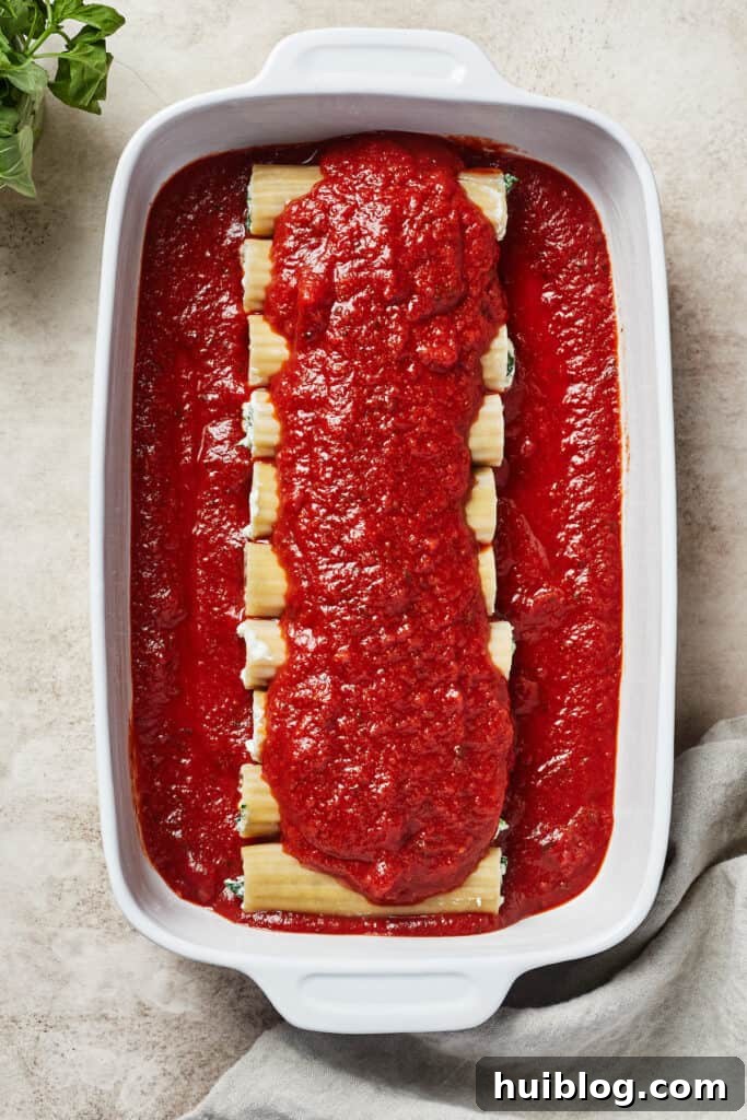 Uncooked manicotti pasta arranged neatly in a baking dish, generously covered in a rich red marinara sauce, ready for the oven.