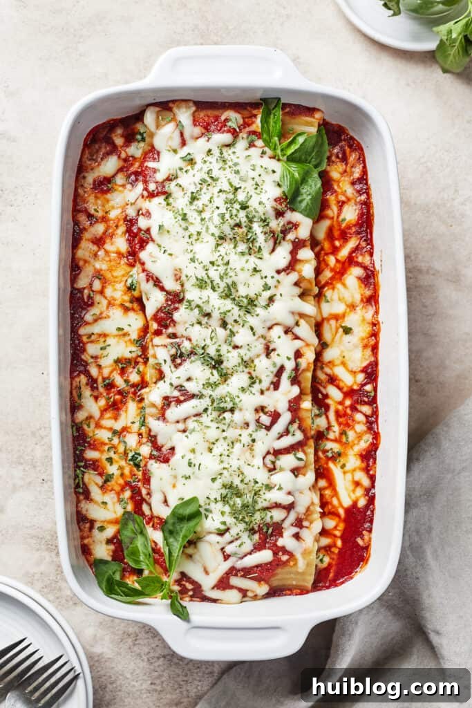 A beautifully baked pasta dish, bubbling with melted cheese and rich marinara, garnished with vibrant fresh herbs, presented in a white casserole dish.