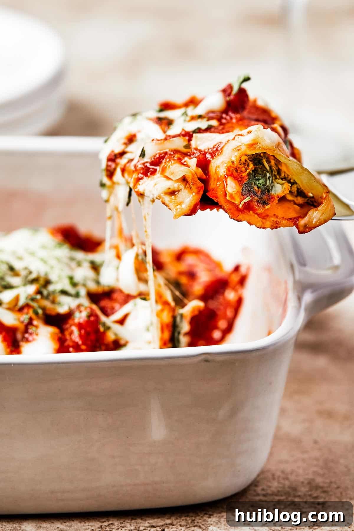 A serving of perfectly baked cheese manicotti being lifted from a large casserole dish with a spatula, showcasing its melted cheese and rich sauce.