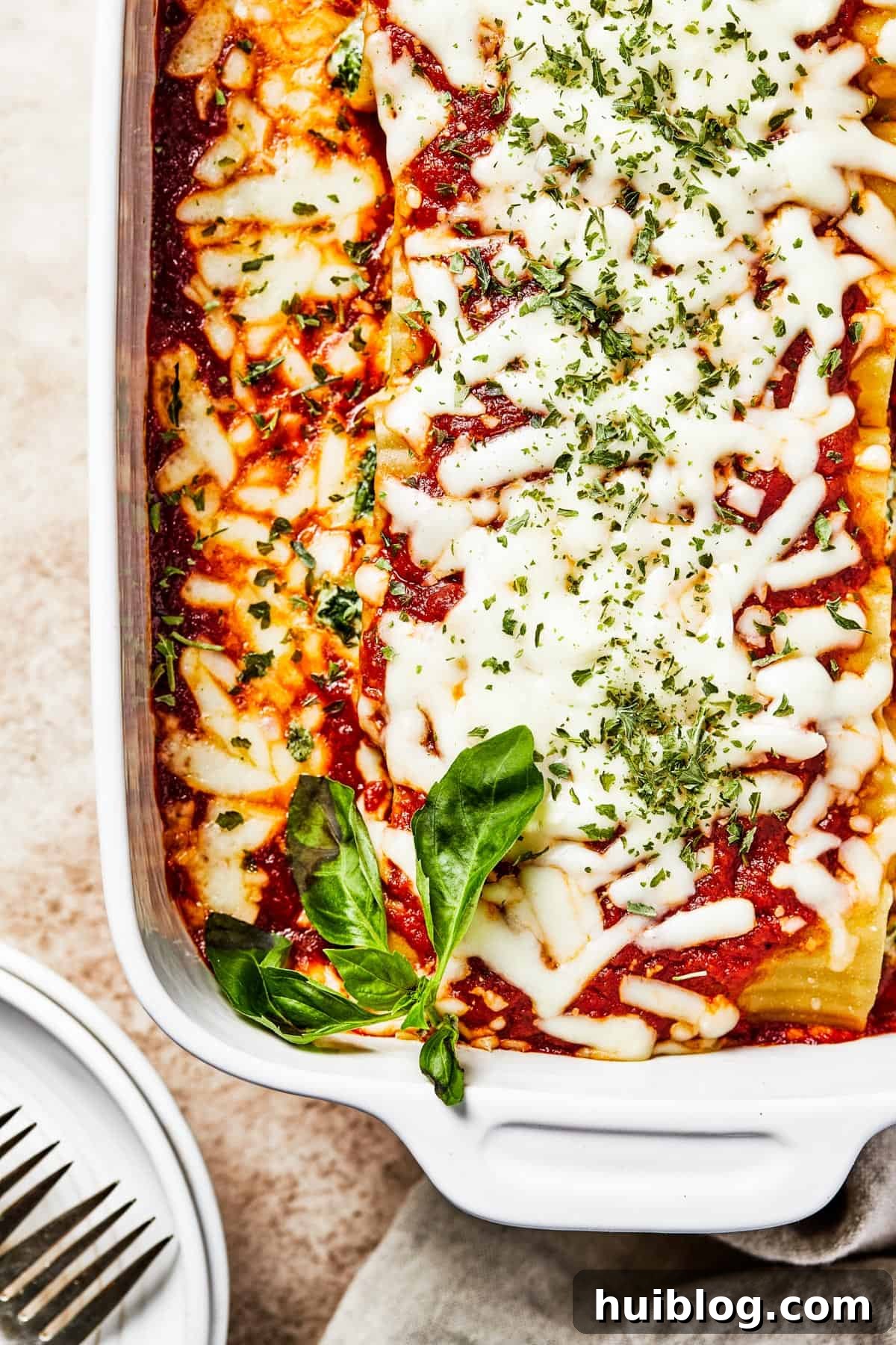 A close-up of a white casserole dish filled with baked pasta, rich marinara sauce, and perfectly melted, bubbly cheese, garnished with fresh herbs.