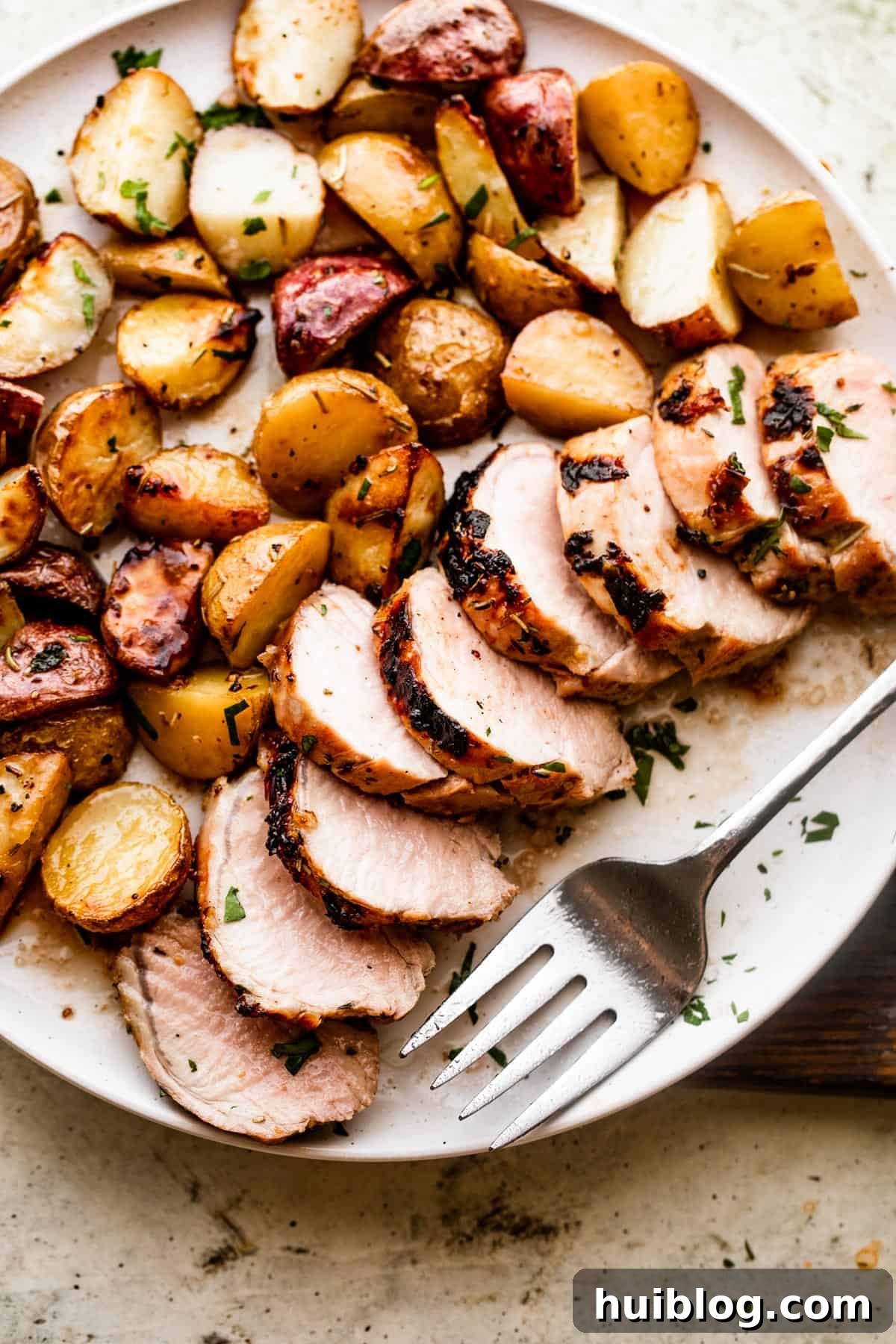 overhead shot of a serving plate with sliced roast pork tenderloin served with colored baby potatoes