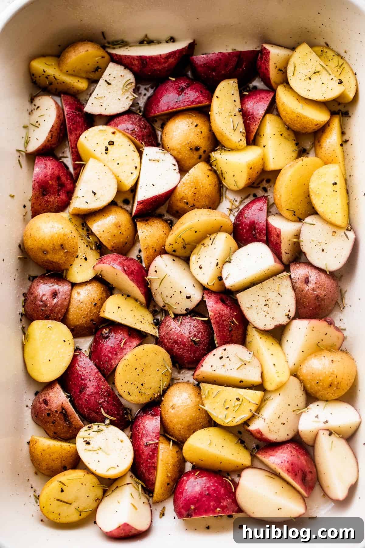 quartered and colorful baby potatoes arranged in a baking dish and seasoned with dried herbs