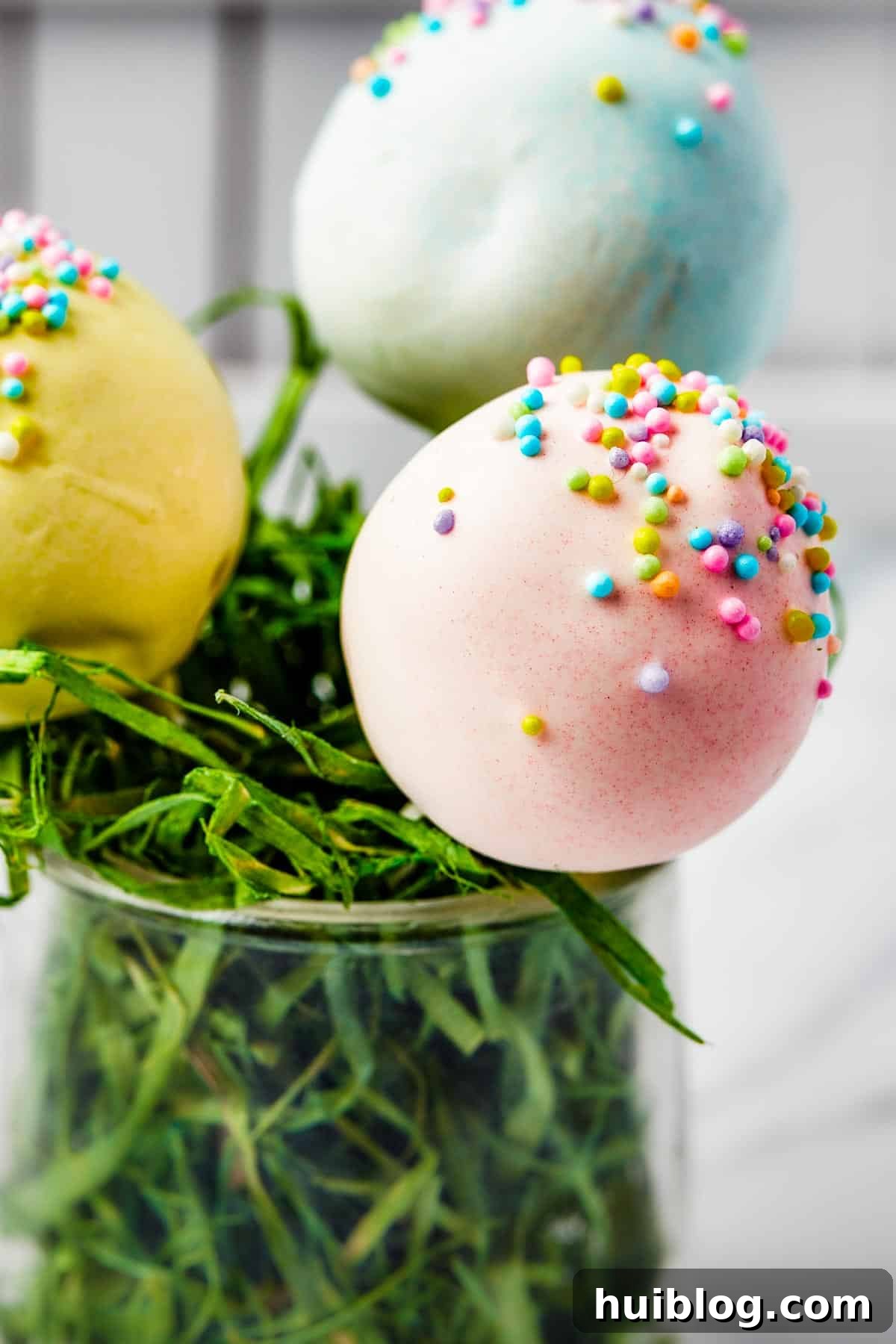 Pastel cake pop lollipops in a white basket filled with festive Easter grass, ready for a celebration.