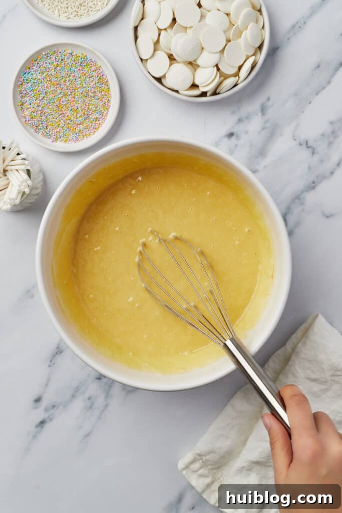 Yellow cake batter in a mixing bowl with a whisk, showcasing the smooth, ready-to-bake consistency.