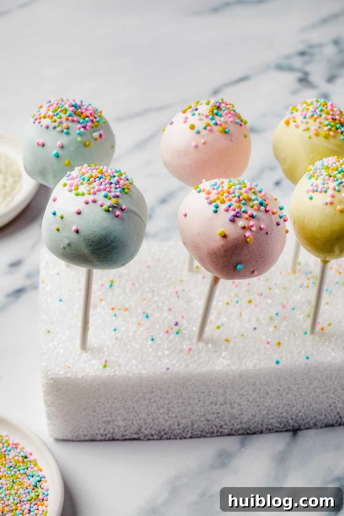 Lollipops cake pops with colorful sprinkles, meticulously drying in a styrofoam block.