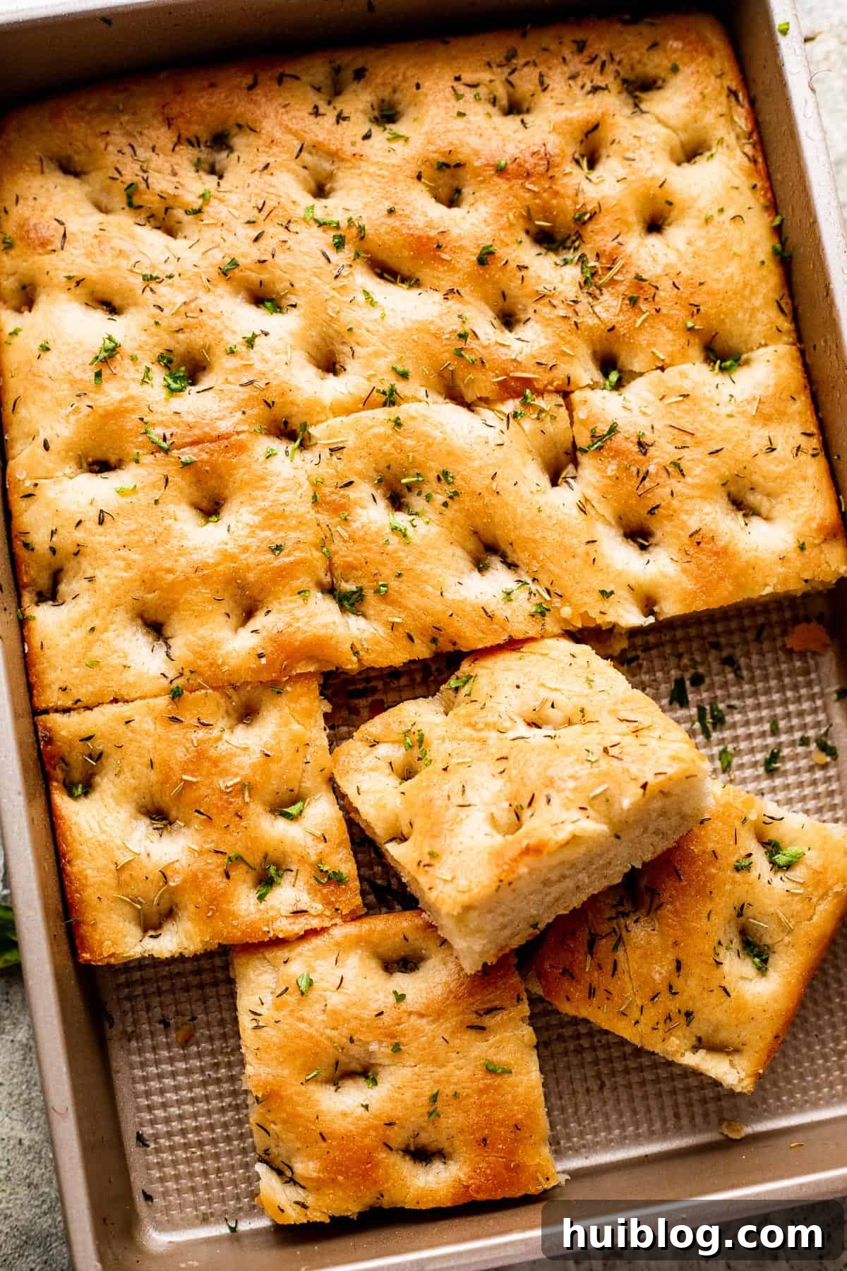 Aromatic Garlic and Herb Focaccia 2 A large pan-sized loaf of focaccia, with four squares of bread cut away, showing its golden-brown crust and airy interior.