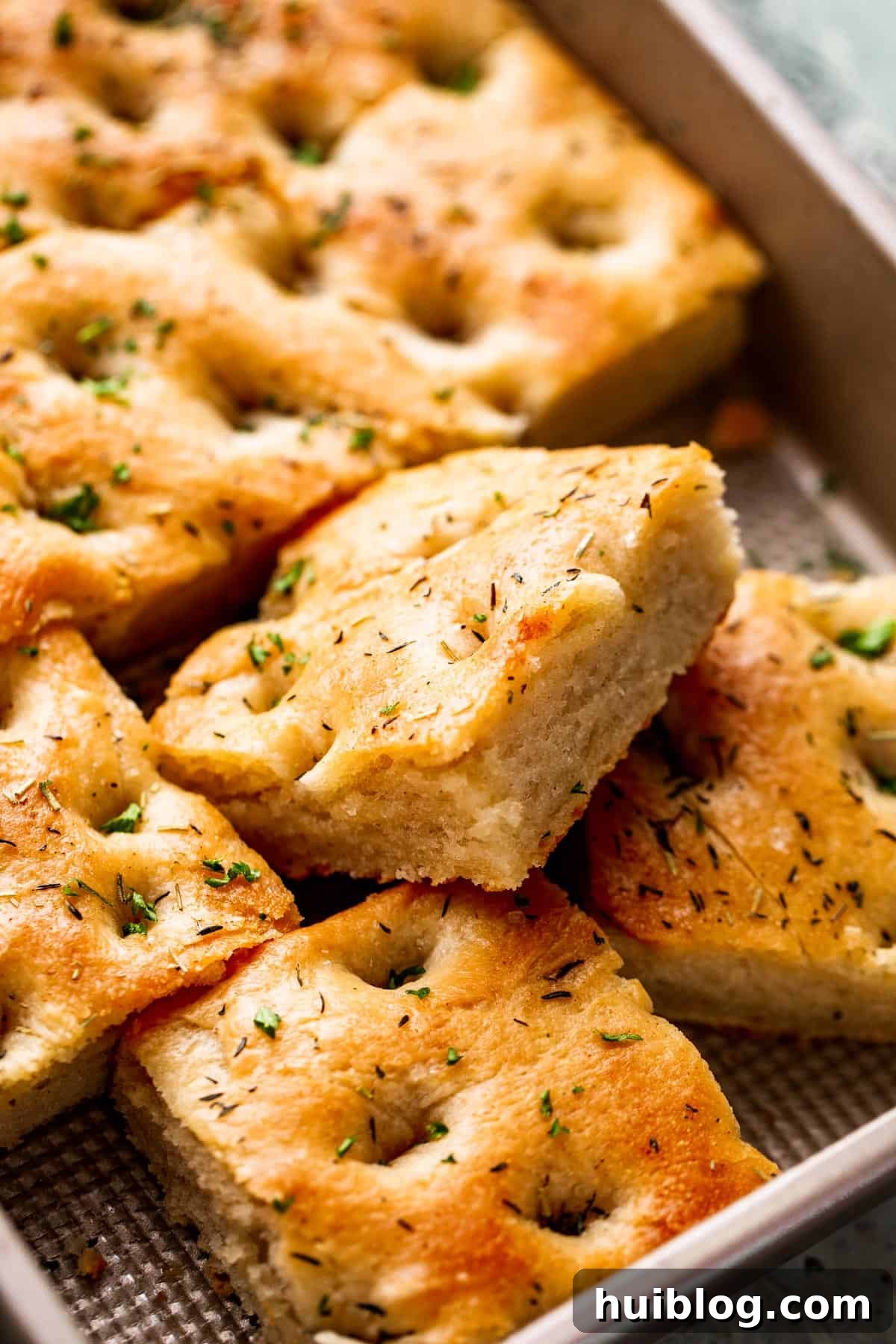 Aromatic Garlic and Herb Focaccia 9 A large pan-sized loaf of focaccia, with four squares of bread already cut away, ready to be served.