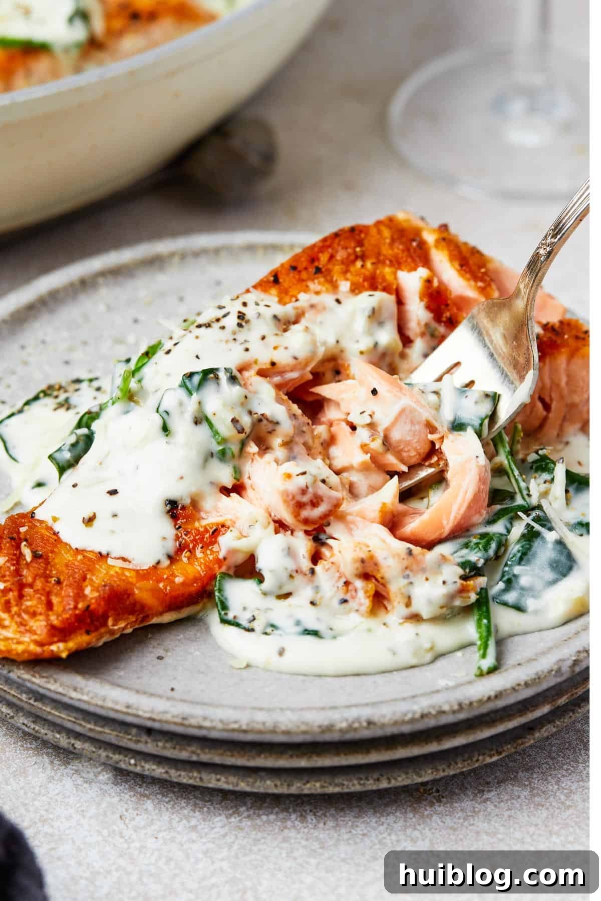 Pan-Seared Salmon with Creamy Spinach 11 A serving of salmon florentine. A bite of the salmon is being lifted toward the camera on a fork.