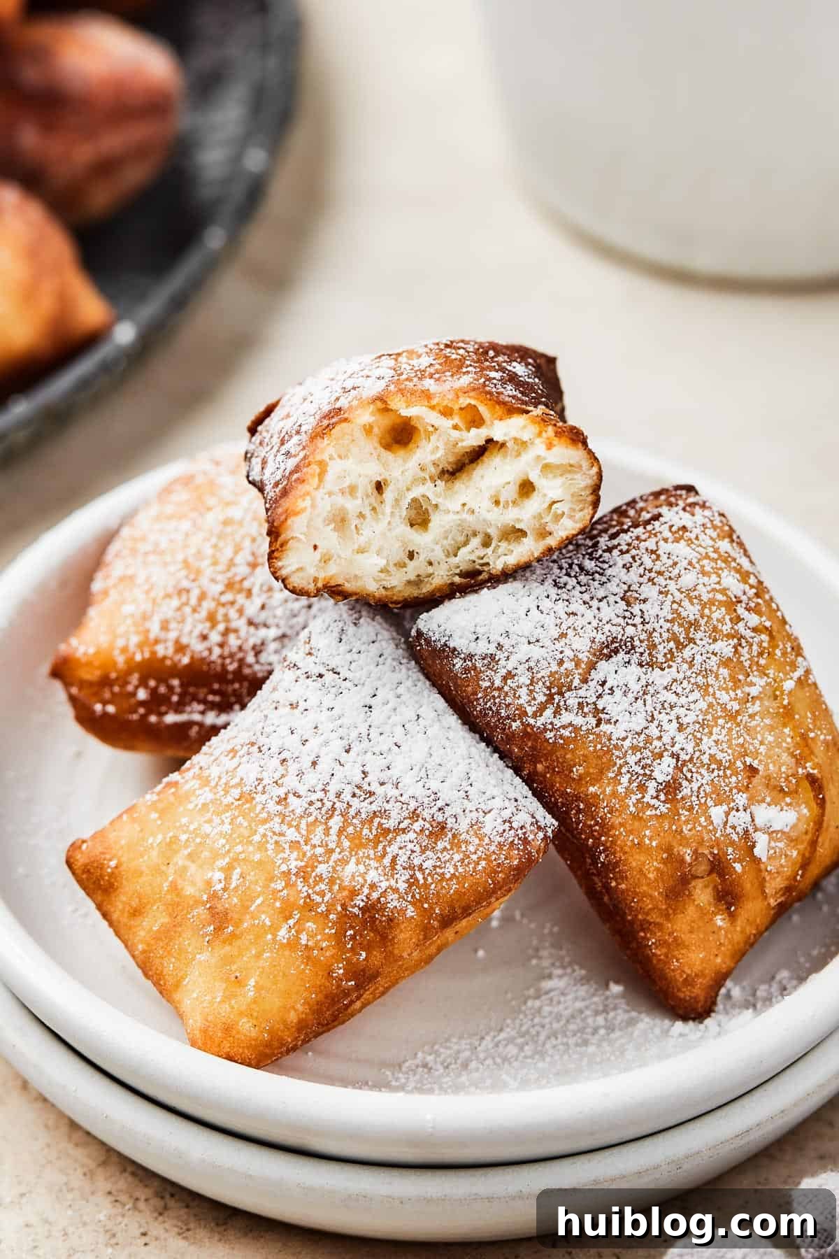 French Quarter Cloud Cakes 11 A plate of homemade square donuts, with one beignet broken in half to beautifully display its fluffy, airy interior texture.
