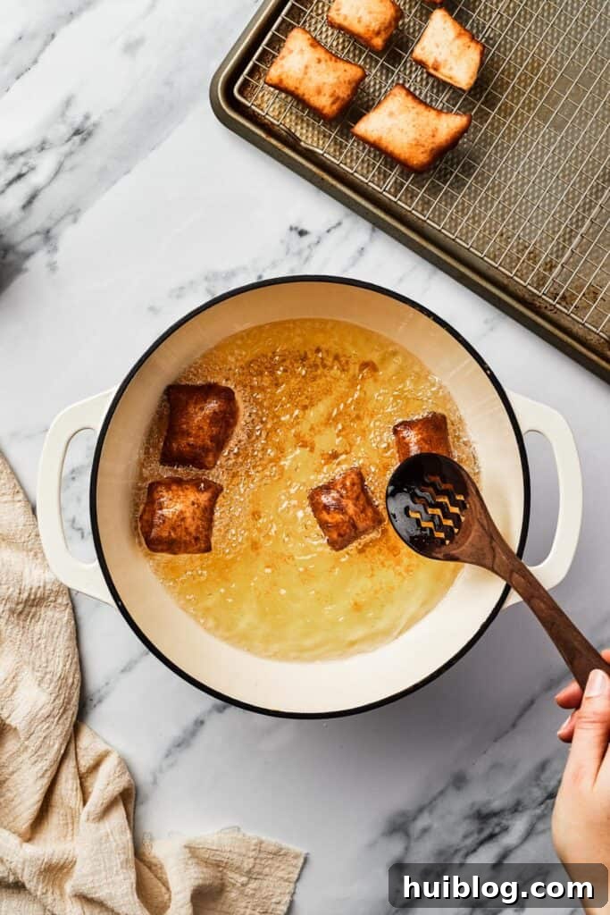 French Quarter Cloud Cakes 8 Golden-brown, puffy squares of fried dough float in a Dutch oven filled with shimmering hot oil, amidst the frying process.