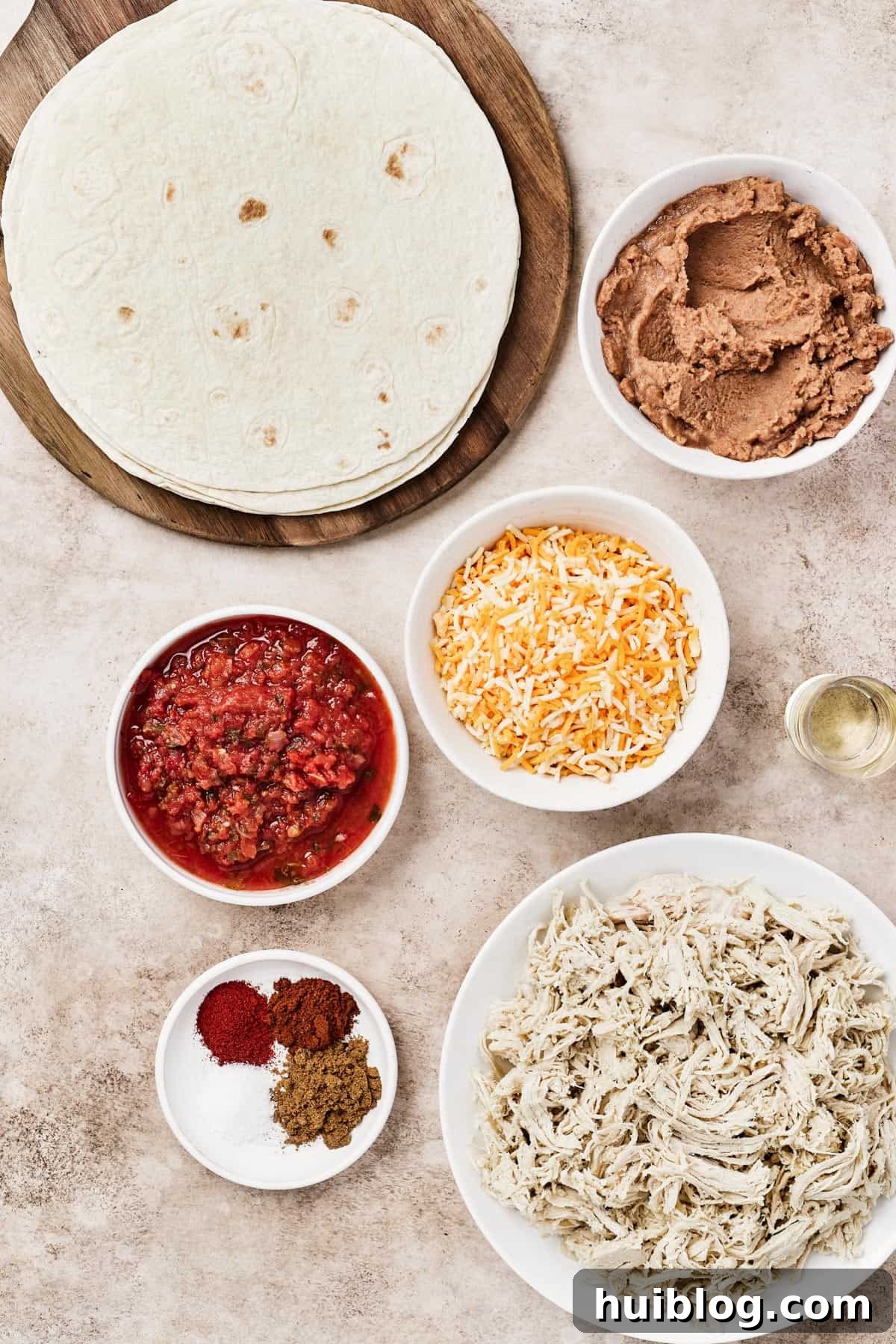 From top left: Tortillas, refried beans, salsa, shredded cheese, oil, spices, shredded chicken.