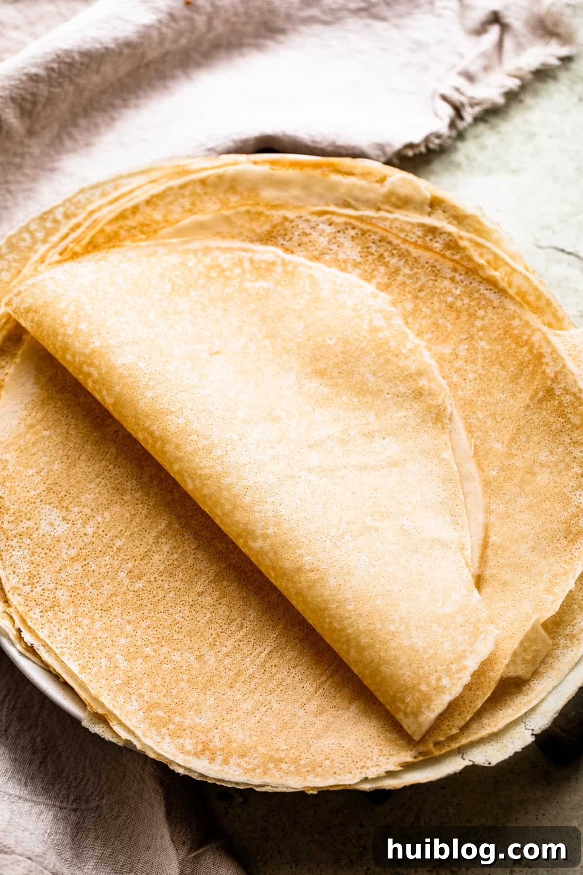Whip Up Perfect French Crepes 4 Freshly made homemade crepes stacked neatly on a white plate, with several folded in half to showcase their delicate texture.