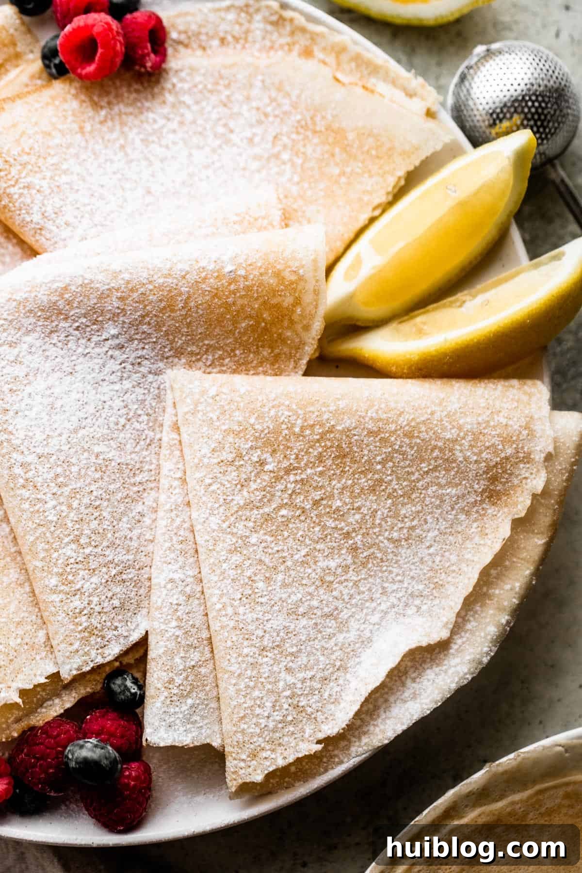 Whip Up Perfect French Crepes 5 Overhead view of three beautifully folded homemade crepes, generously dusted with powdered sugar, presented on a rustic wooden board.