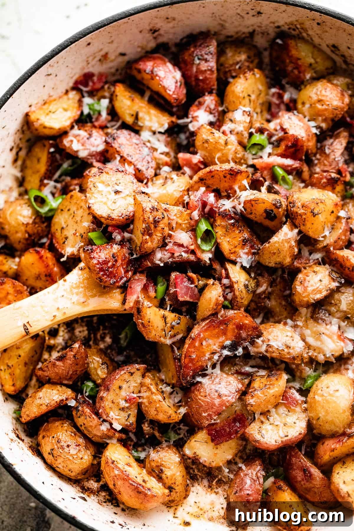 overhead shot of golden roasted potatoes with crispy bacon bits and melted cheese in a white skillet, garnished with fresh green onions.