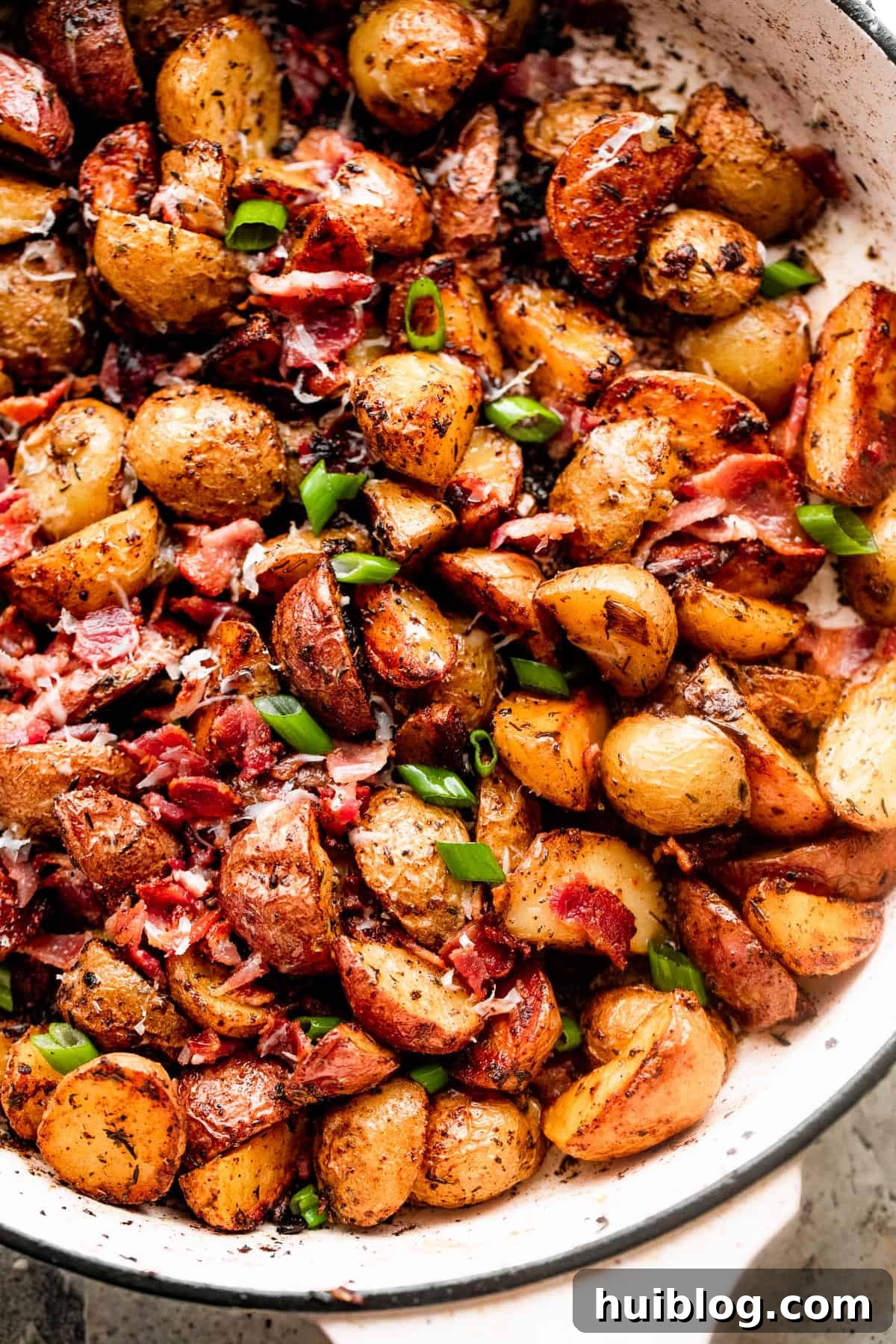 overhead shot of roasted potatoes with bacon and cheese, garnished with fresh green onions, in a white skillet.