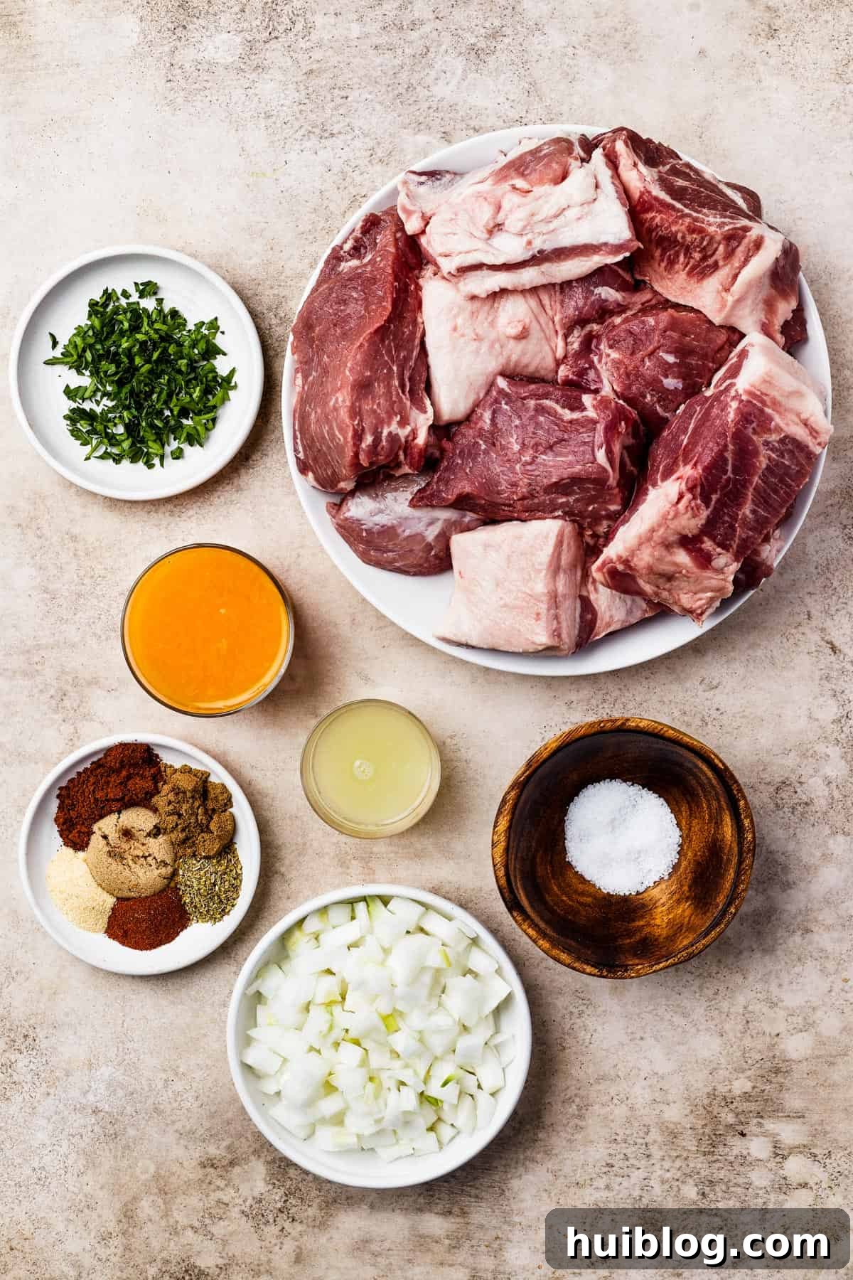 From top left: Chopped cilantro, raw pork butt, orange juice, lime juice, seasonings, salt, and white onion, laid out for the recipe.