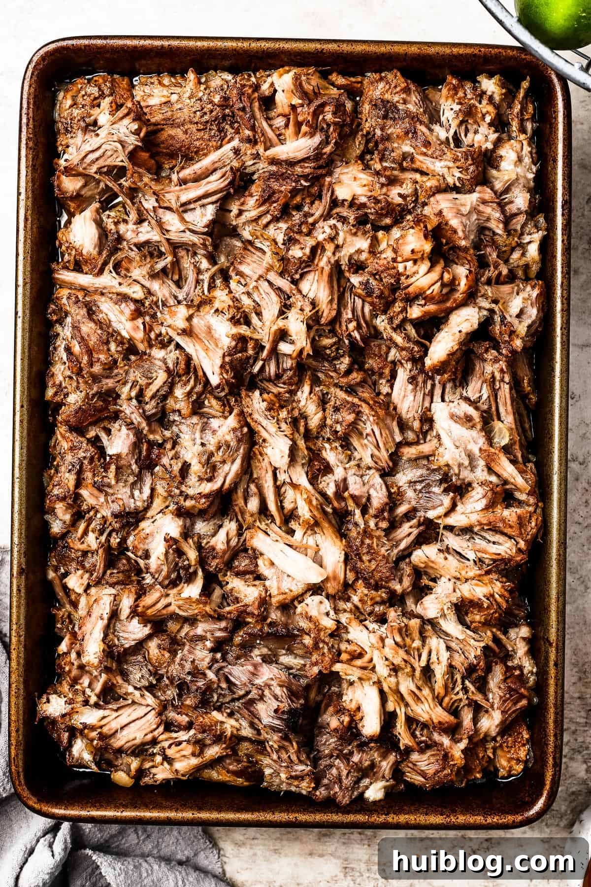 Perfectly browned and shredded pork carnitas spread on a baking sheet after broiling.