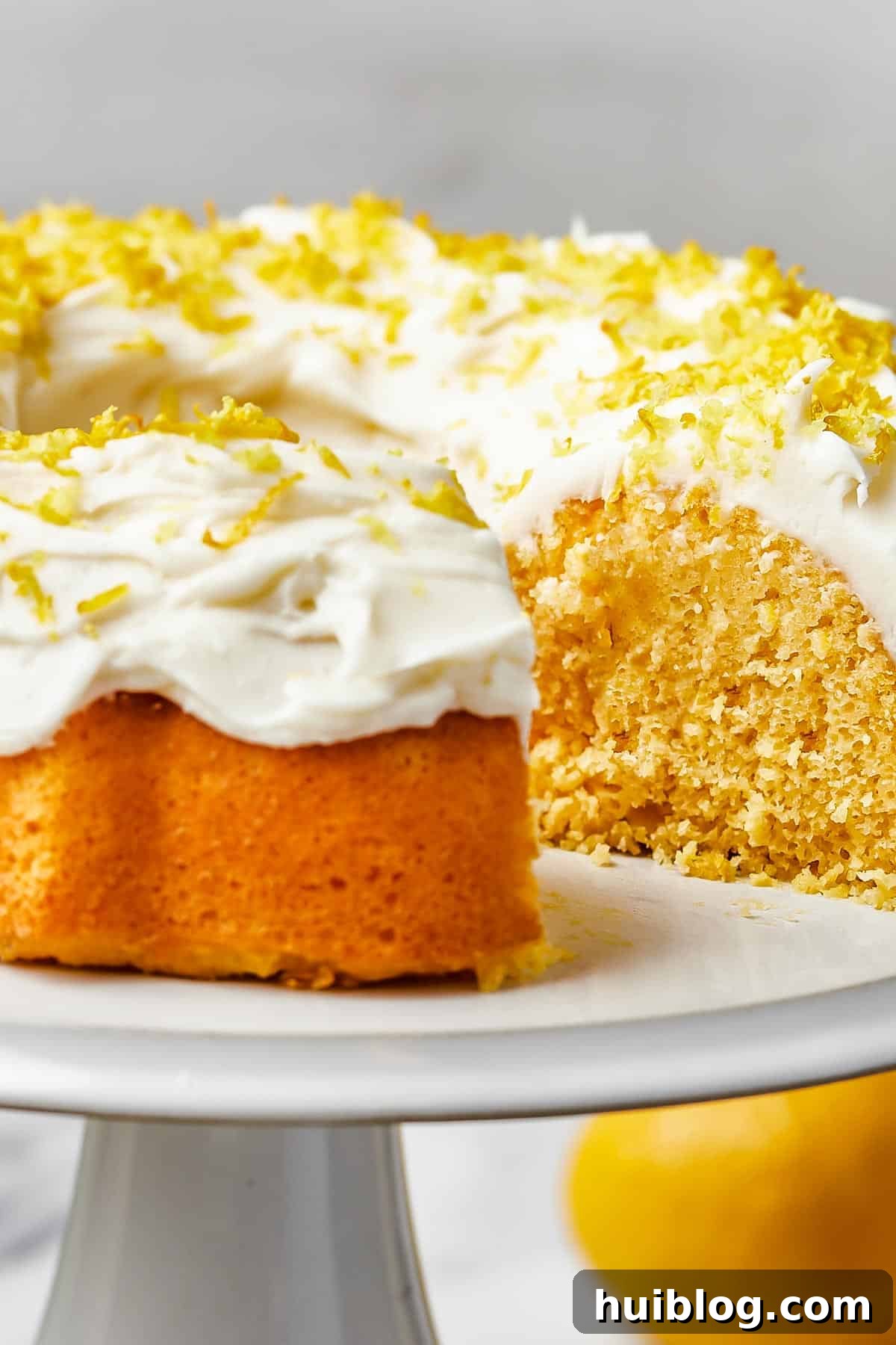 Close up shot of a lemon bundt cake, generously iced with thick, creamy frosting and artfully topped with bright lemon zest, ready to be served.