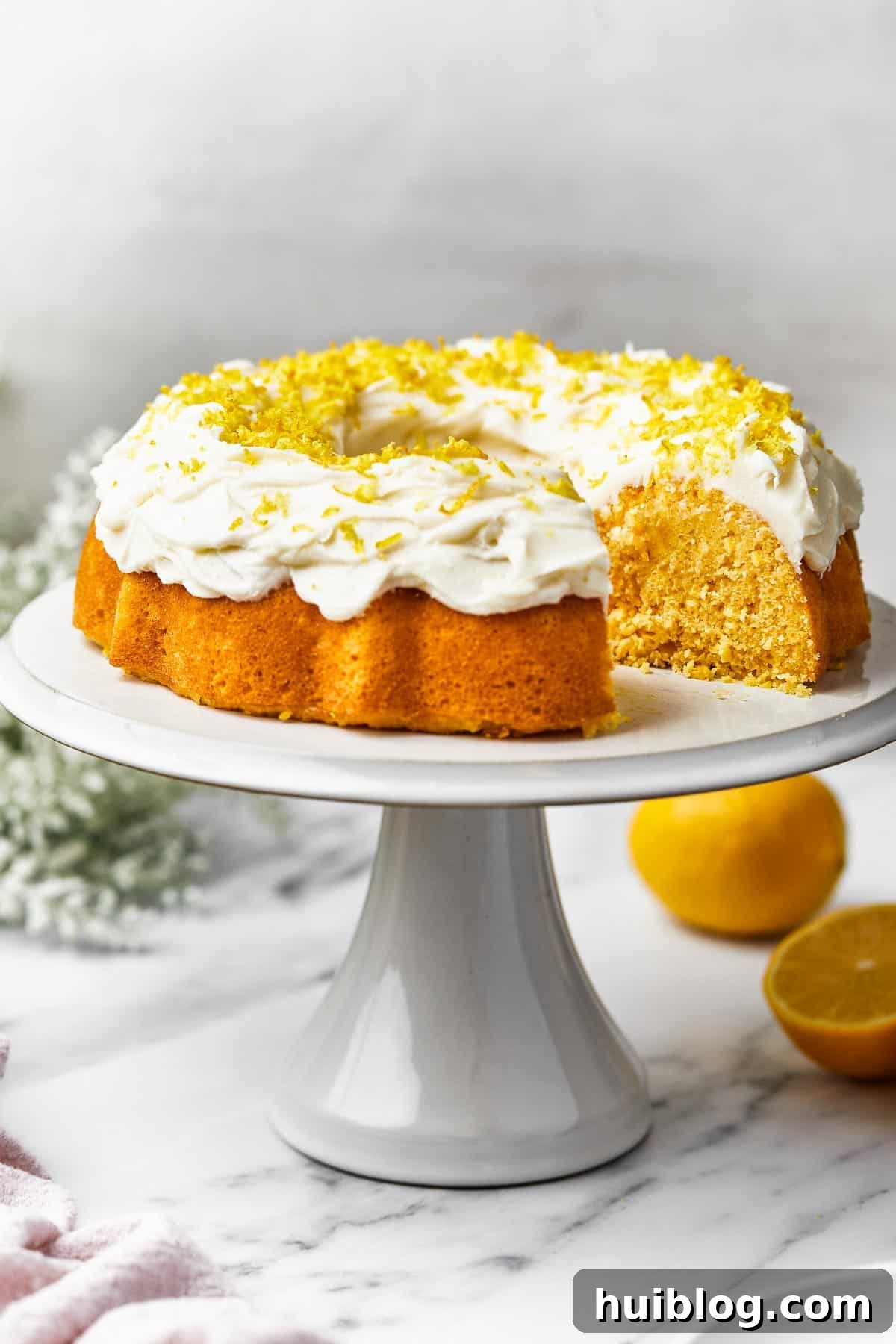 A beautifully baked lemon Bundt cake rests on a pristine white platter, with one perfect slice carefully removed, revealing its moist, tender interior.