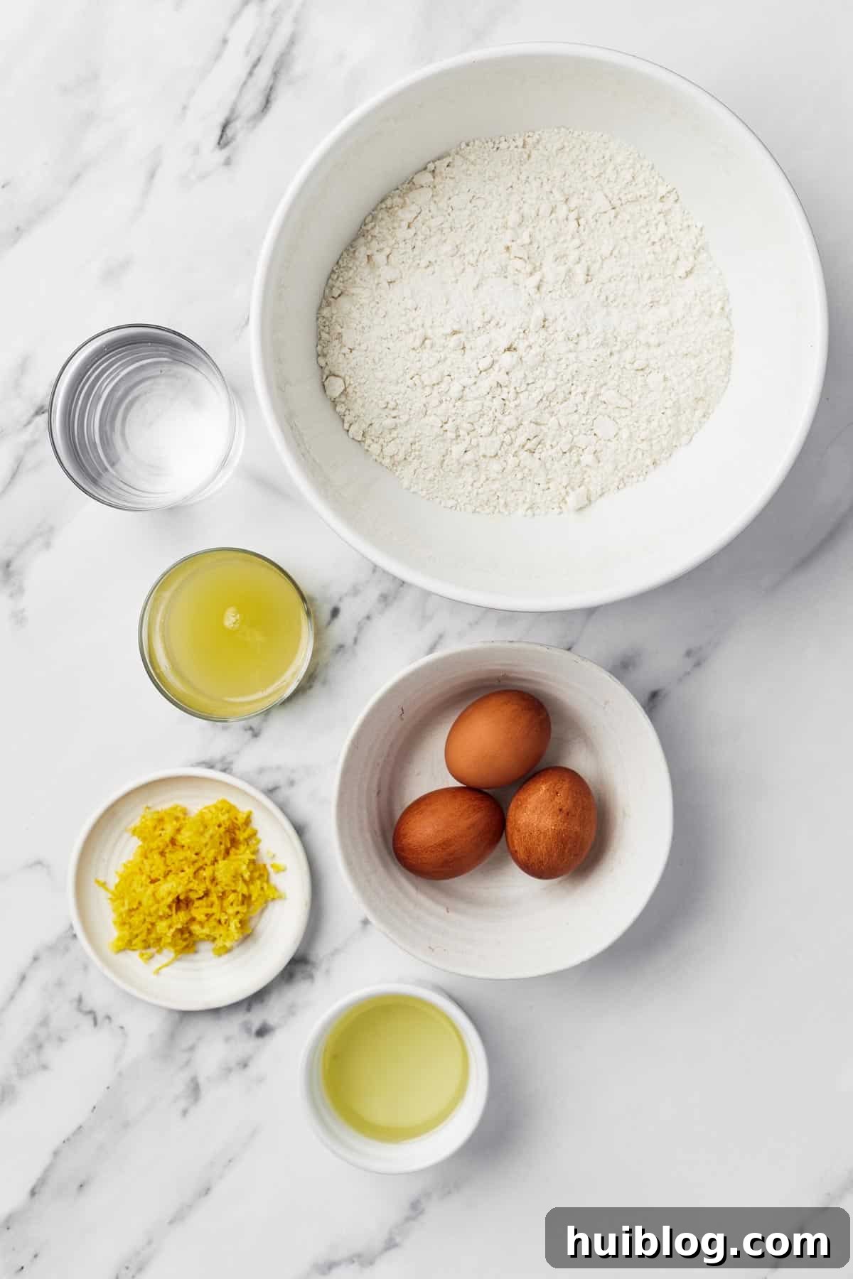 A vibrant flat lay of essential lemon bundt cake ingredients: fresh water, a box of cake mix, cooking oil, farm-fresh eggs, bright yellow lemon zest, and freshly squeezed lemon juice.