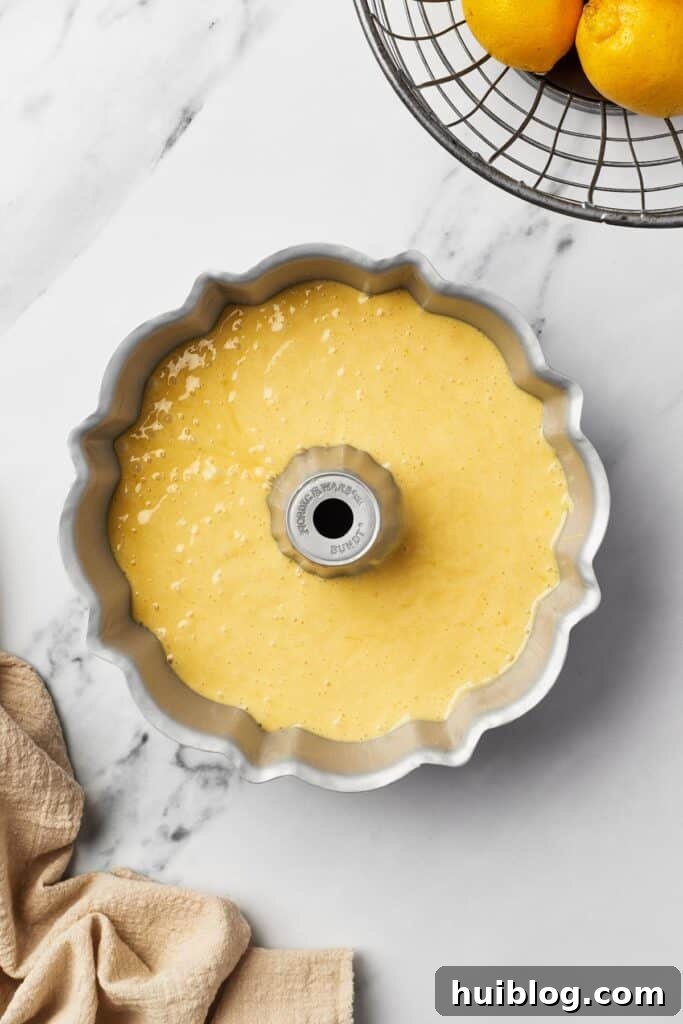 A classic fluted Bundt pan, perfectly greased and filled with a smooth, bright yellow cake batter, ready for baking.