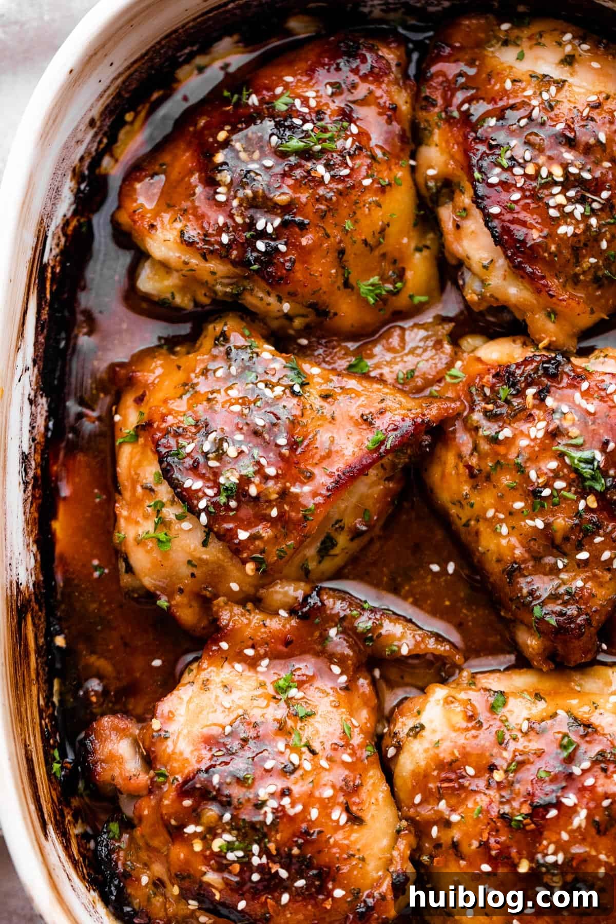 overhead shot of a baking dish with six honey garlic baked chicken thighs garnished with sesame seeds.