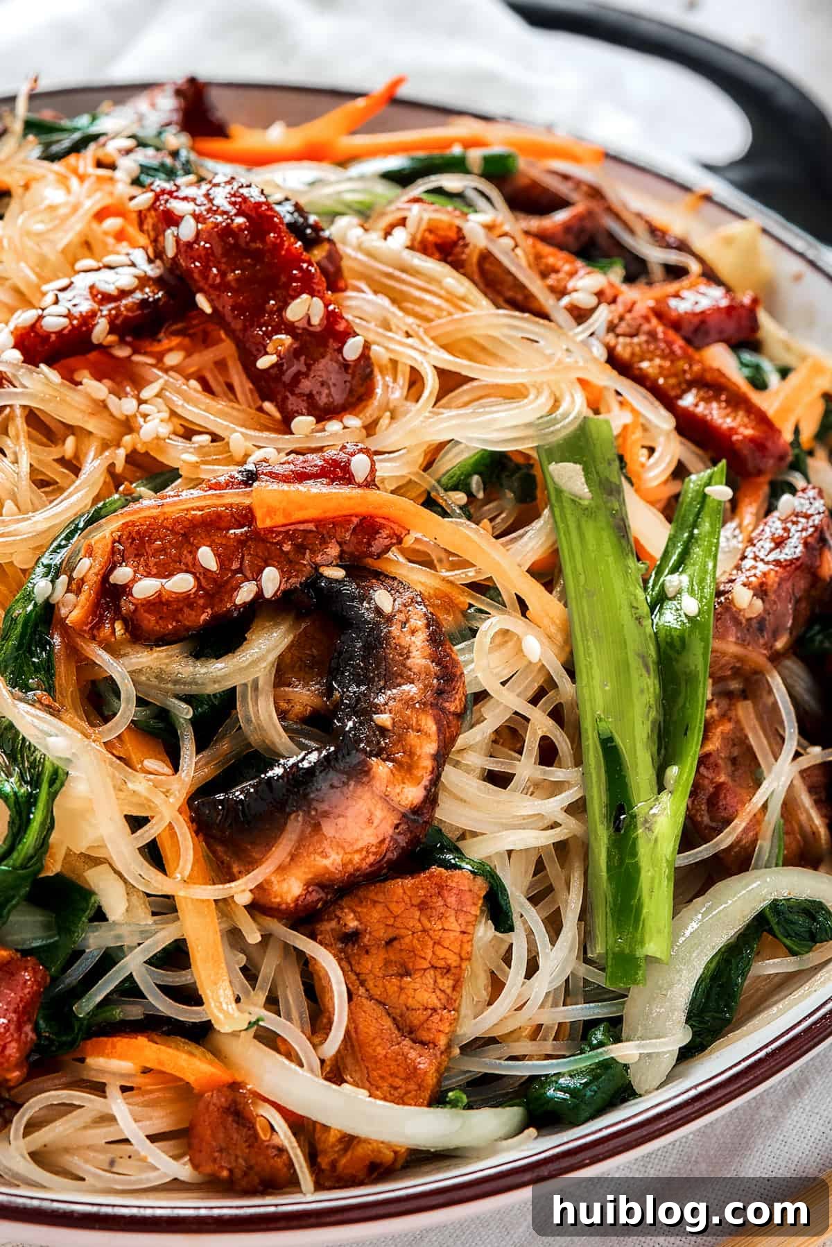 The Art of Serving Perfect Japchae A shallow dish of vibrant Korean Beef Japchae (glass noodle stir fry), richly garnished with toasted sesame seeds, ready to be served.