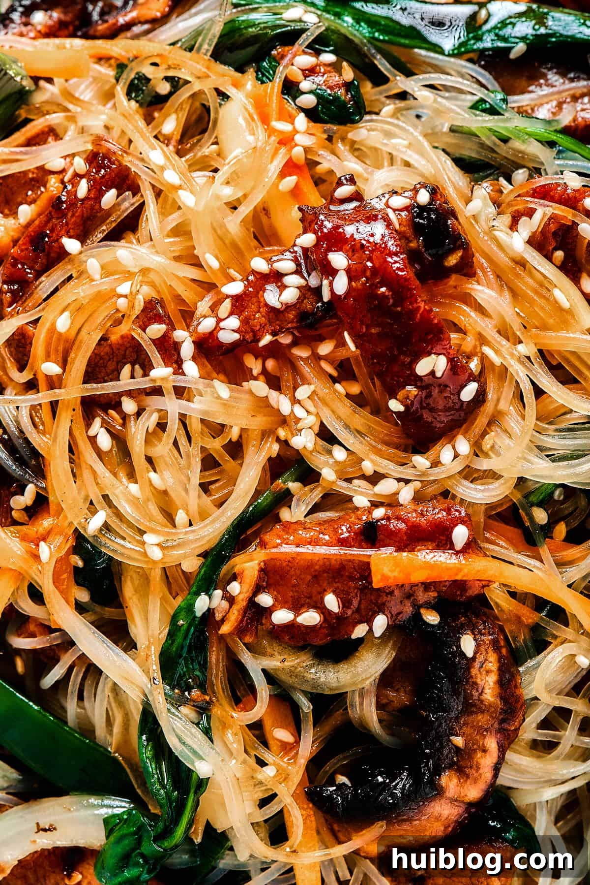 A Close Look at the Irresistible Japchae Close-up shot of Japchae (Korean glass noodle stir fry) richly garnished with toasted sesame seeds, highlighting the vibrant colors and textures of the dish.