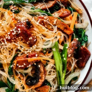 overhead shot of a shallow dish of beef noodle stir fry, garnished with sesame seeds.