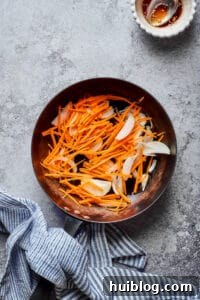 Korean Beef and Glass Noodle Japchae 4 Matchstick carrots and thinly sliced onions stir-frying in a skillet, turning translucent and tender-crisp.