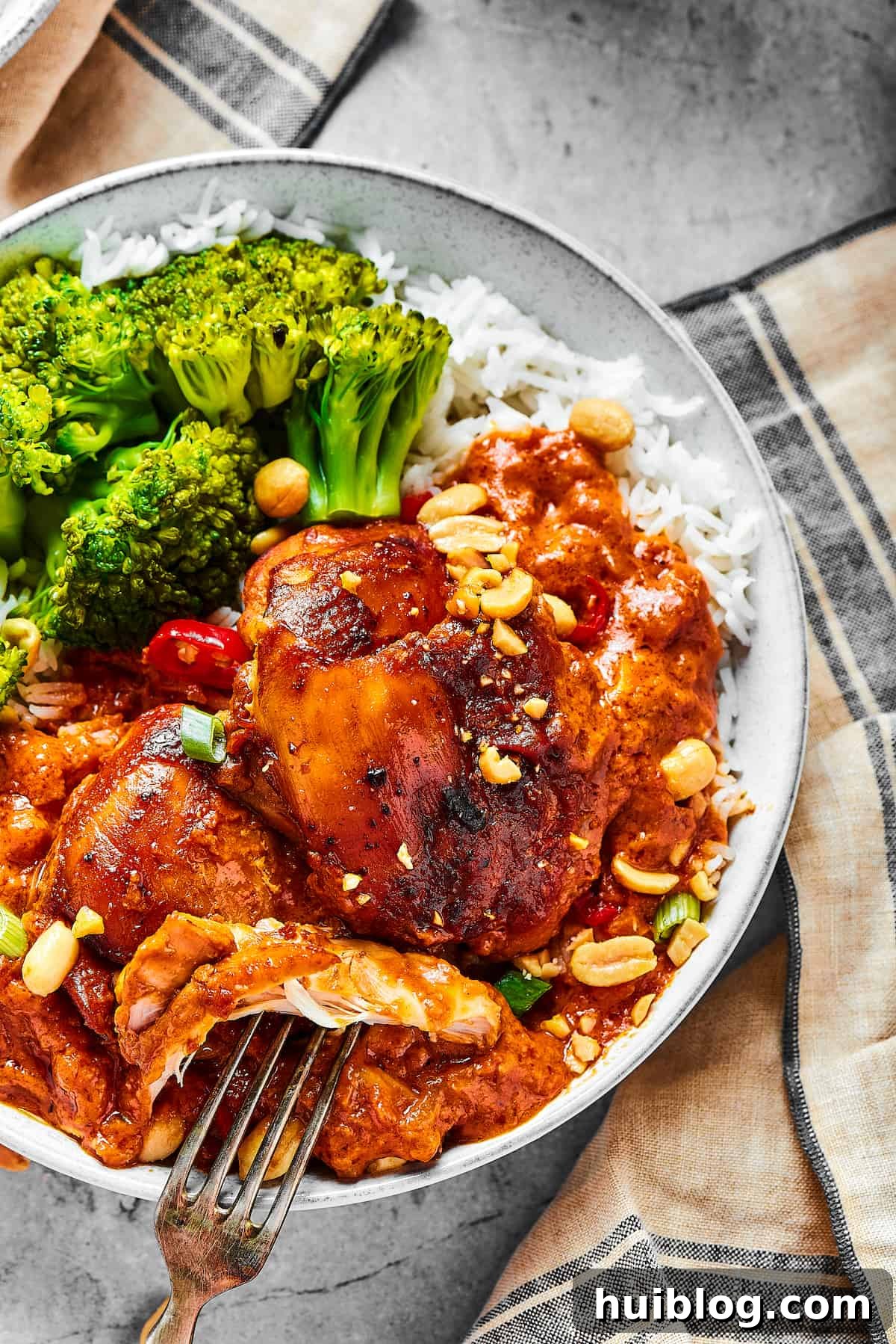 Close-Up of Tender Peanut Butter Chicken An overhead shot showing a single, perfectly cooked chicken thigh bathed in a rich peanut sauce, with a fork lifting a succulent piece, ready to be enjoyed.