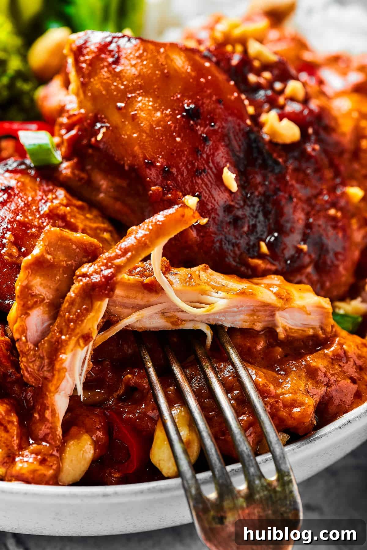 Simple Peanut Butter Chicken with crushed tomatoes, soy sauce, and garlic is a breeze to make. Serve this saucy chicken over rice, noodles, or cauliflower rice, and watch it disappear! A close-up shot of a chicken thigh cooked in peanut sauce, with a fork pulling away a bite.