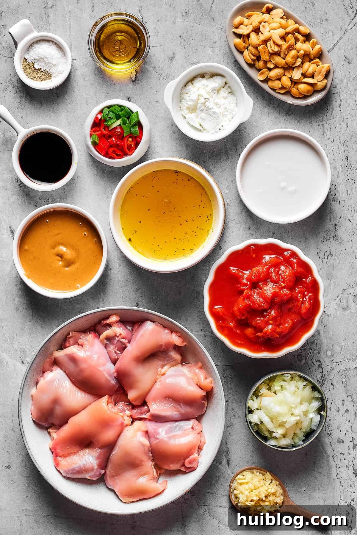 Fresh Ingredients for Flavorful Peanut Butter Chicken An overhead shot showcasing all the fresh and pantry ingredients laid out for Peanut Butter Chicken. From left to right: Salt, olive oil, roasted peanuts, soy sauce, sliced chilies and green onions, cornstarch, creamy peanut butter, chicken stock, rich coconut milk, raw chicken thighs, crushed tomatoes, chopped onion, and minced garlic.