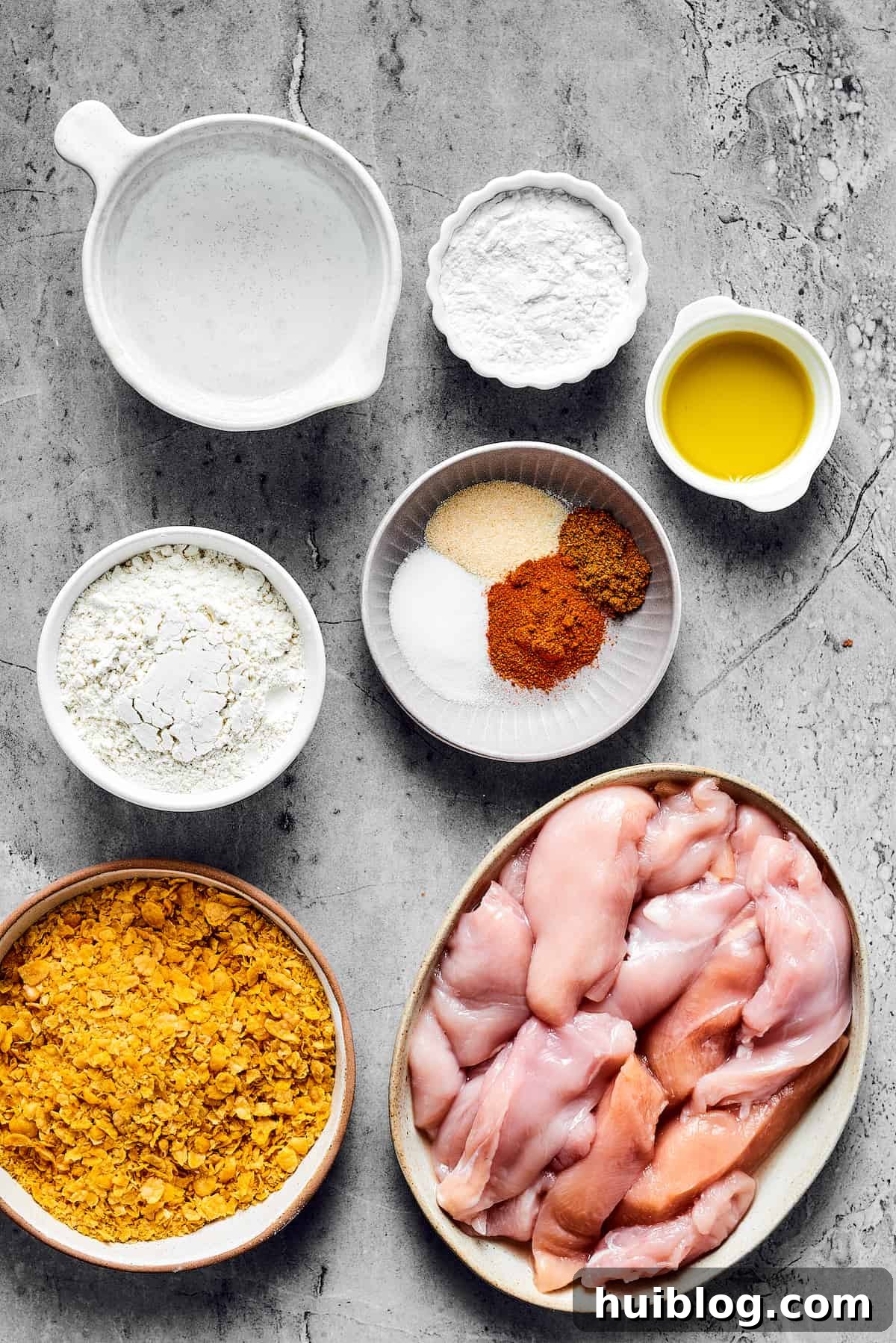 From top: Water, tapioca flour, olive oil, all-purpose flour, seasonings, corn flakes, chicken breast strips – all ingredients for Air Fryer Chicken Tempura.