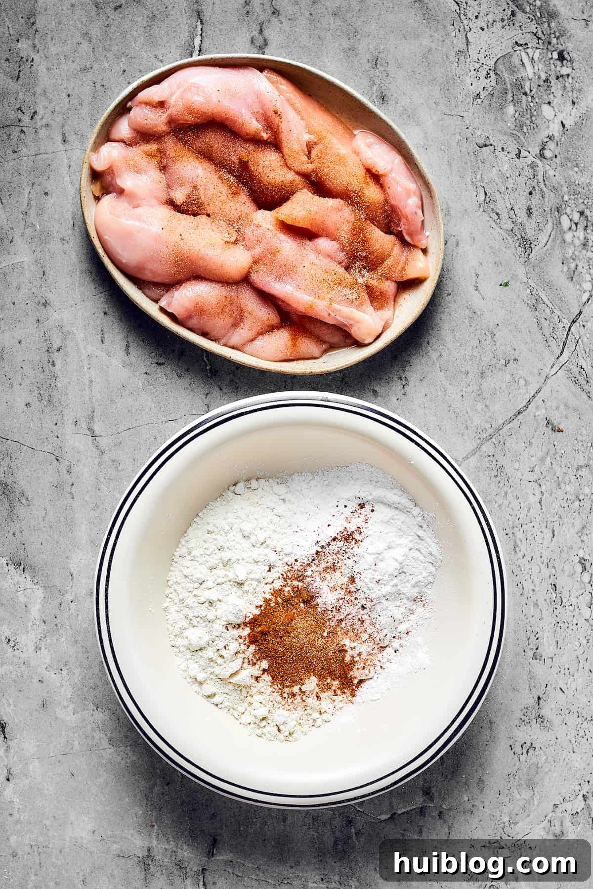 A dish of raw, seasoned chicken strips next to a bowl of seasoned flour, ready for coating.