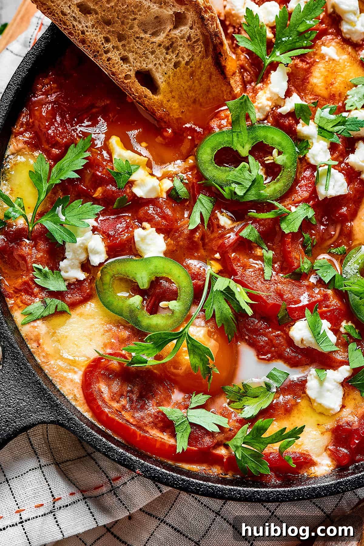 Shakshuka in a cast-iron skillet, with a baguette slice dipped in the sauce.