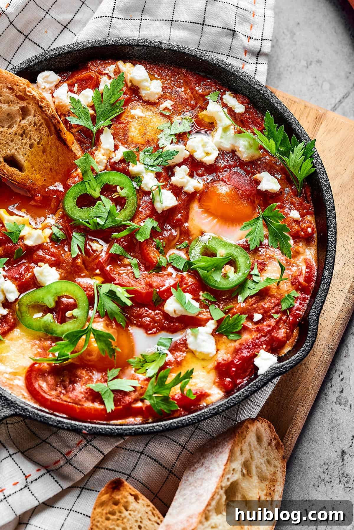 Overhead shot of shakshuka in a cast-iron skillet, with toasted baguette.