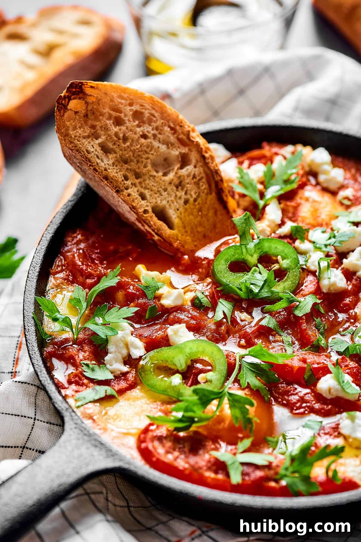 A slice of toasted bread dipped in chunky tomato sauce and poached eggs, garnished with jalapeno and feta cheese.