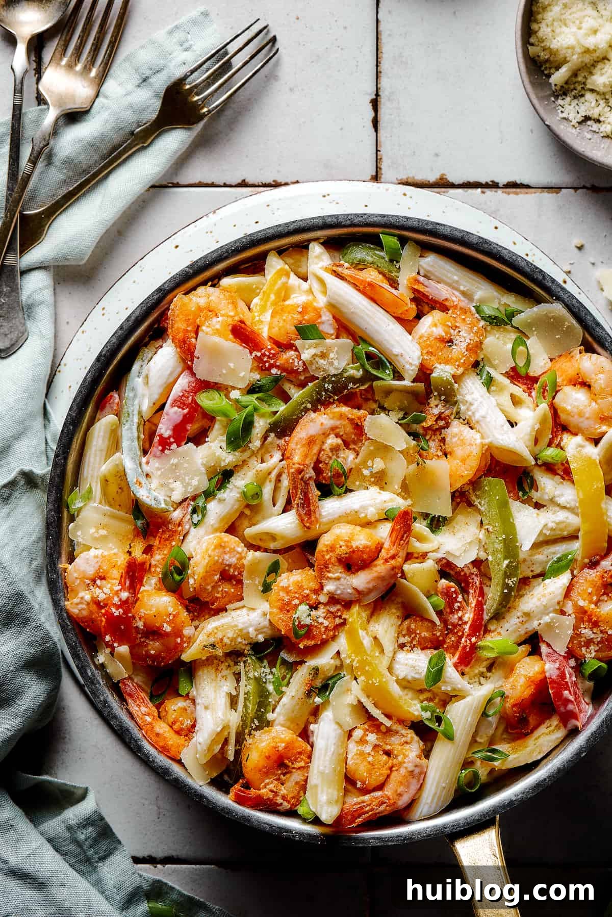 A skillet of Rasta pasta on a countertop, garnished with green onions and fresh herbs.