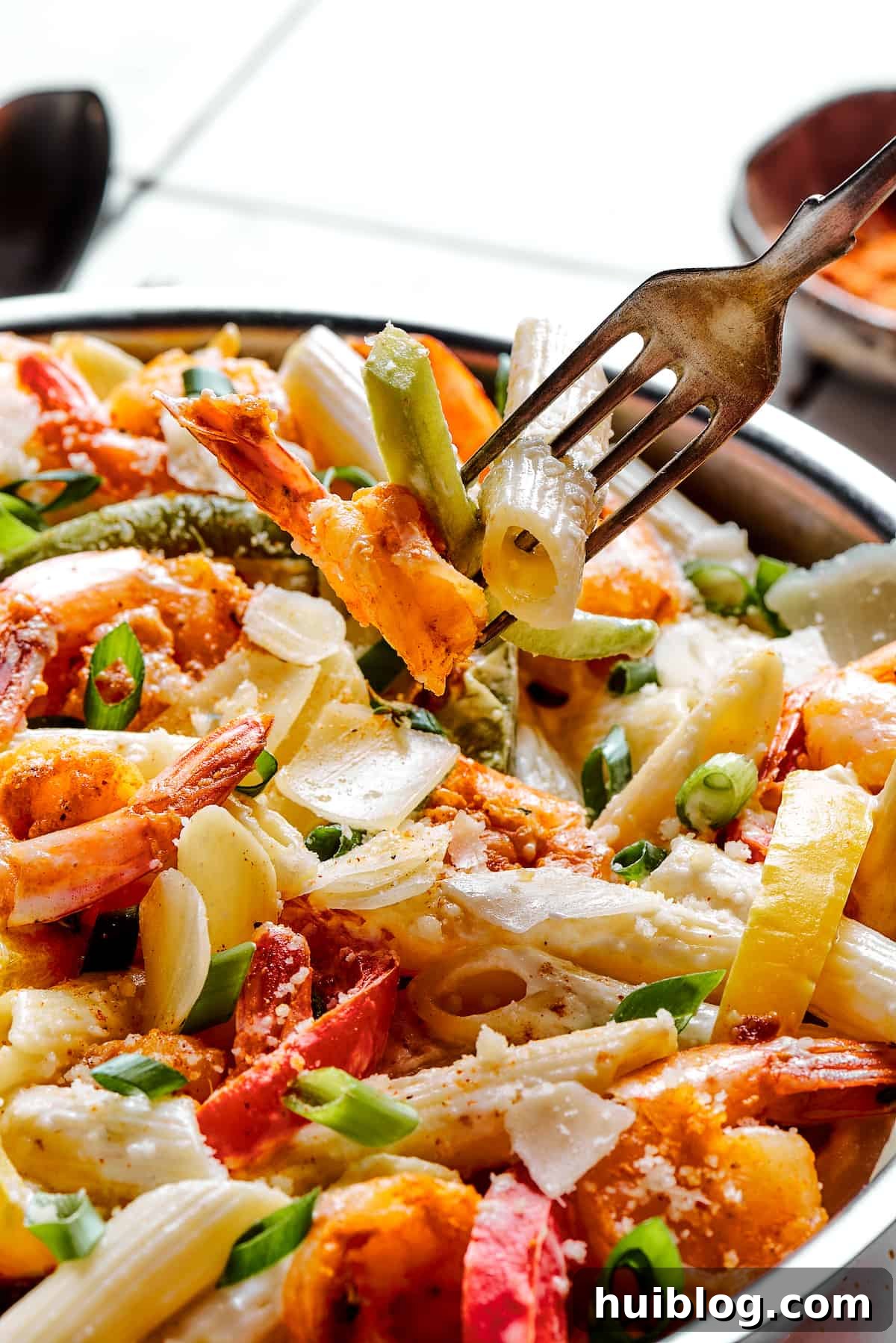 A fork lifting a piece of pasta, shrimp, and bell pepper from a creamy Rasta Pasta dish, emphasizing its appetizing texture.