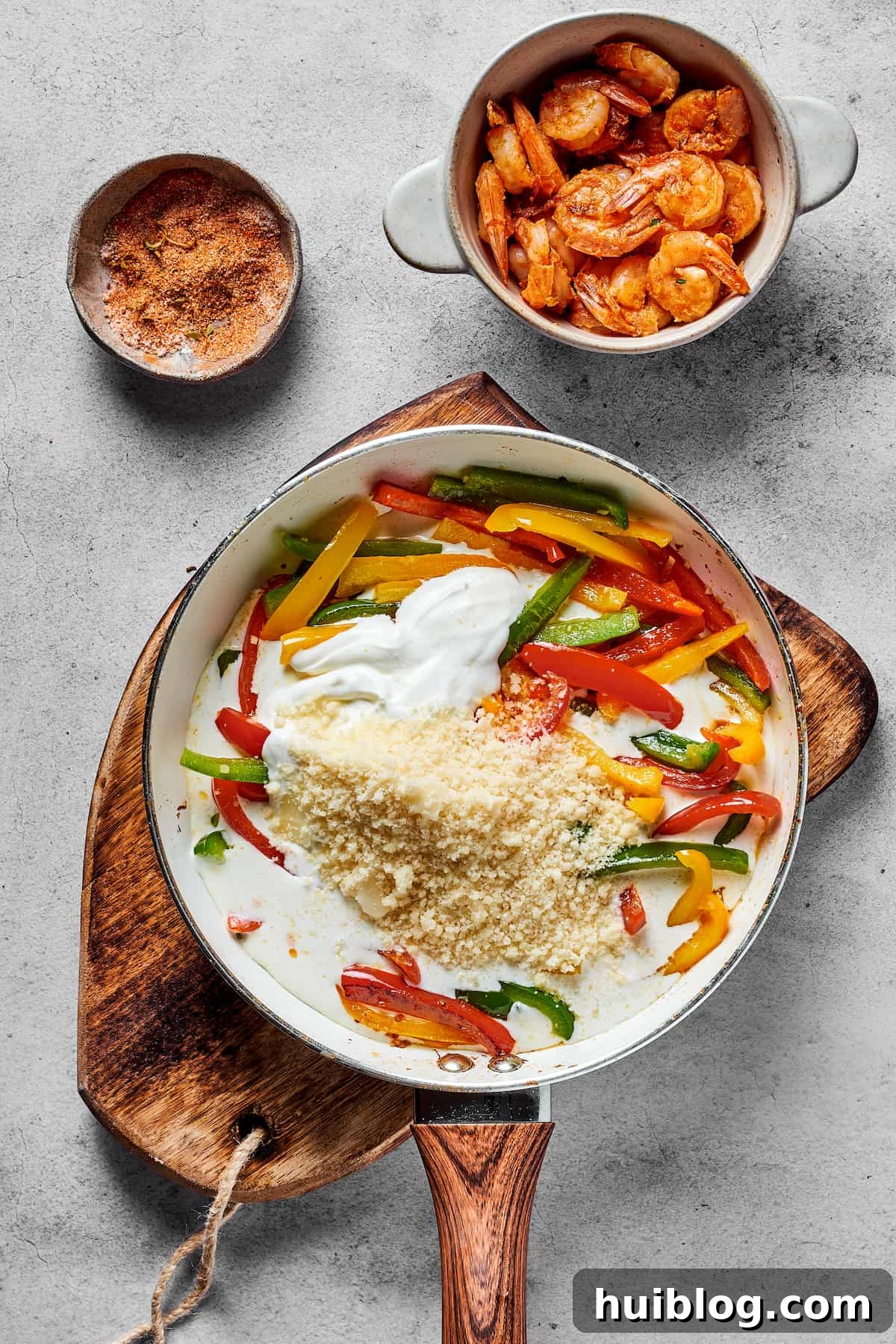 Bell peppers, Parmesan cheese, heavy cream, and cream cheese being stirred together in a skillet to form the creamy Rasta Pasta sauce.
