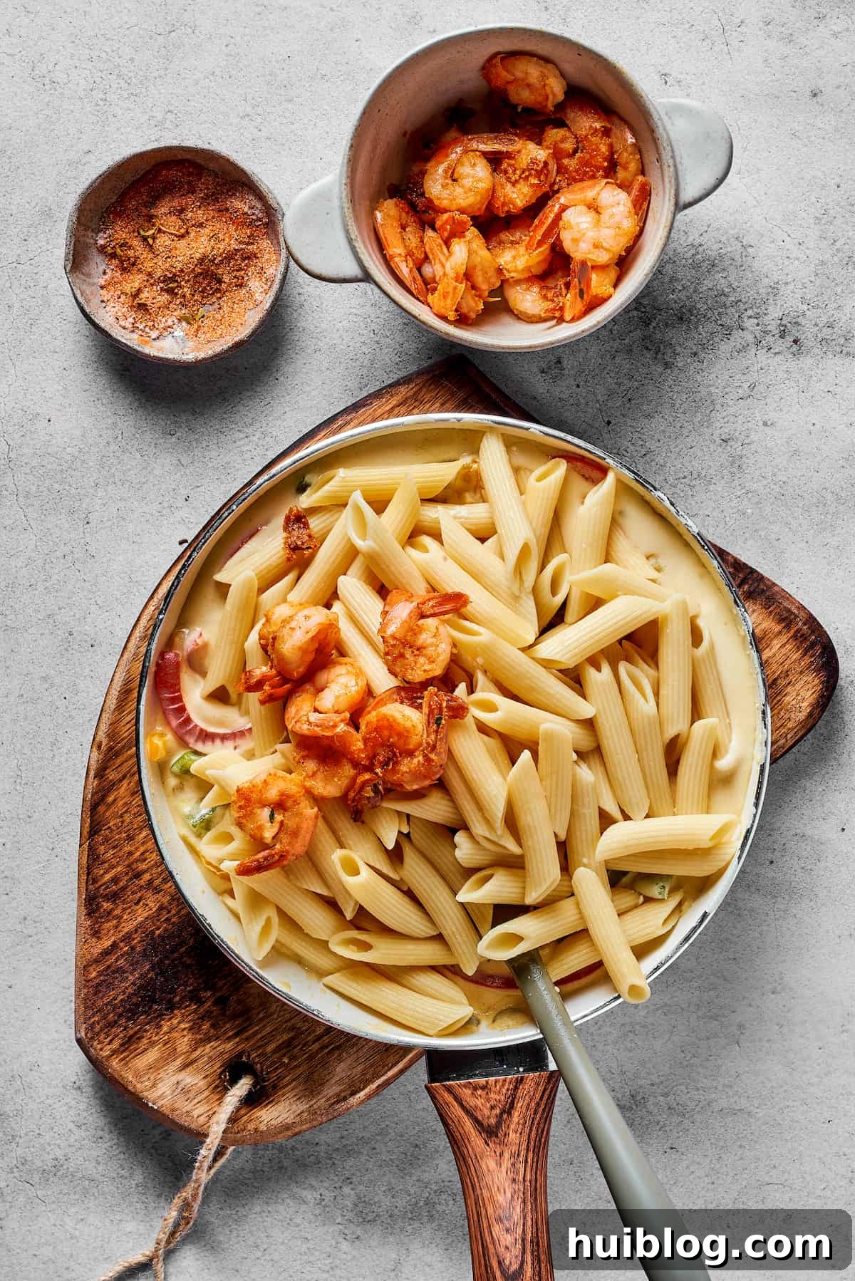 Cooked shrimp and penne pasta being mixed into a skillet of creamy Rasta Pasta sauce with bell peppers.