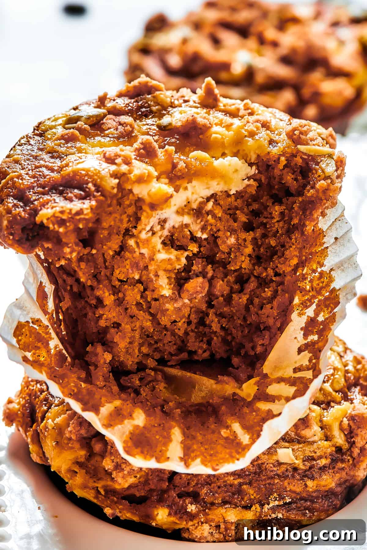 Pumpkin Cream Cheese Muffins are a heavenly mix of spiced pumpkin cake and smooth cream cheese swirl, with a buttery, streusel-like topping. A baked pumpkin muffin, broken cleanly in half, with its paper muffin cup delicately peeled away to reveal the moist interior and vibrant cream cheese swirl.