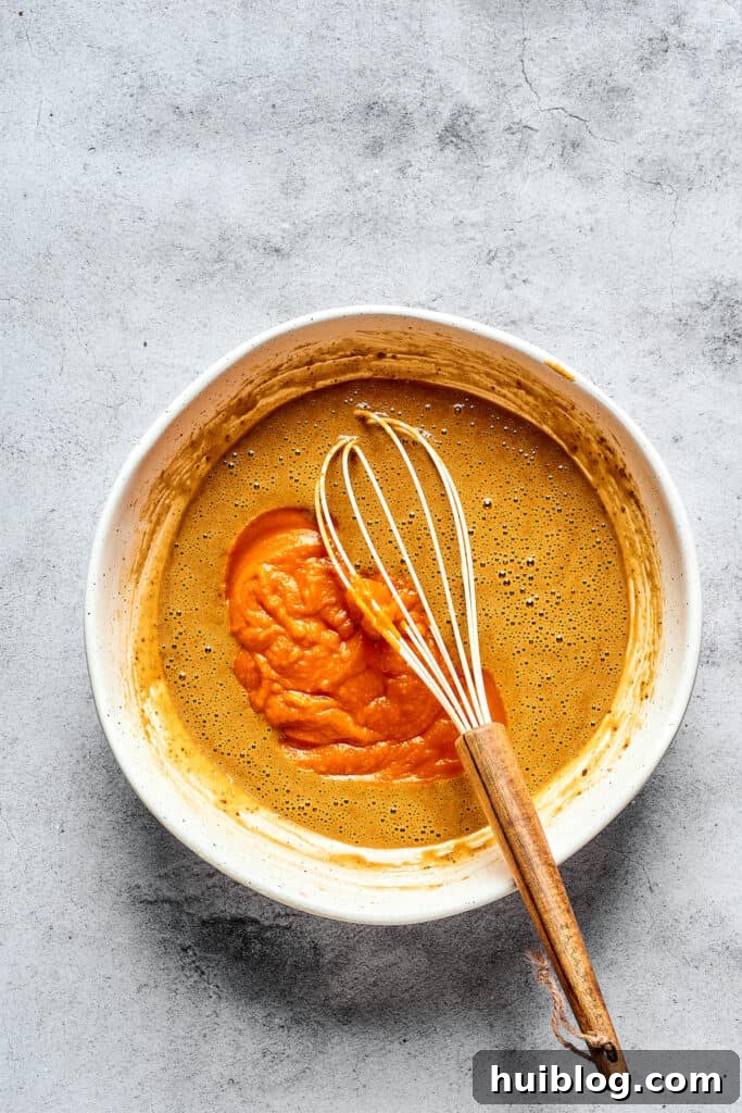 Swirled Pumpkin Cream Cheese Muffins 2 Wet muffin batter ingredients in a mixing bowl with a whisk, showing the vibrant orange pumpkin puree being incorporated.