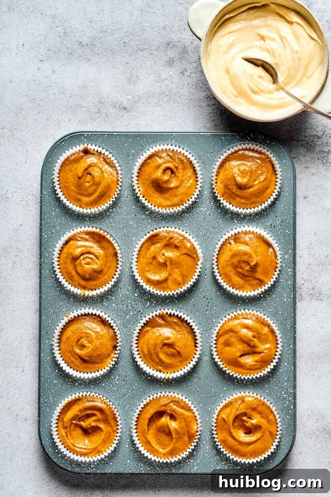 Swirled Pumpkin Cream Cheese Muffins 5 A muffin tin with paper liners filled three-quarters full with pumpkin muffin batter, ready for the cream cheese swirl.