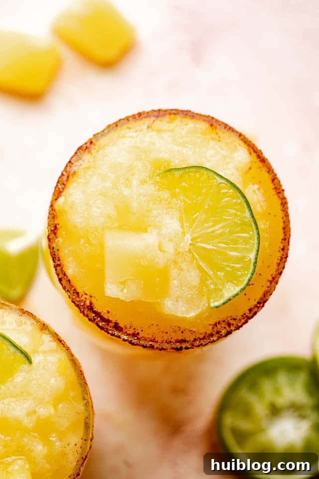 A top-down view of a single frozen pineapple margarita, perfectly blended and garnished, showcasing its inviting texture and chili-salt rim.